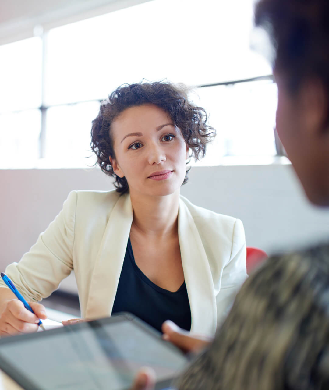 A woman sitting at a table, using a pen and a tablet for work or study purposes.