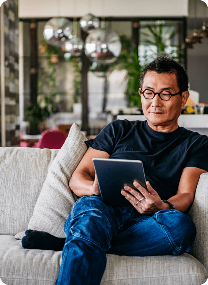 Middle aged man reads tablet on couch. 