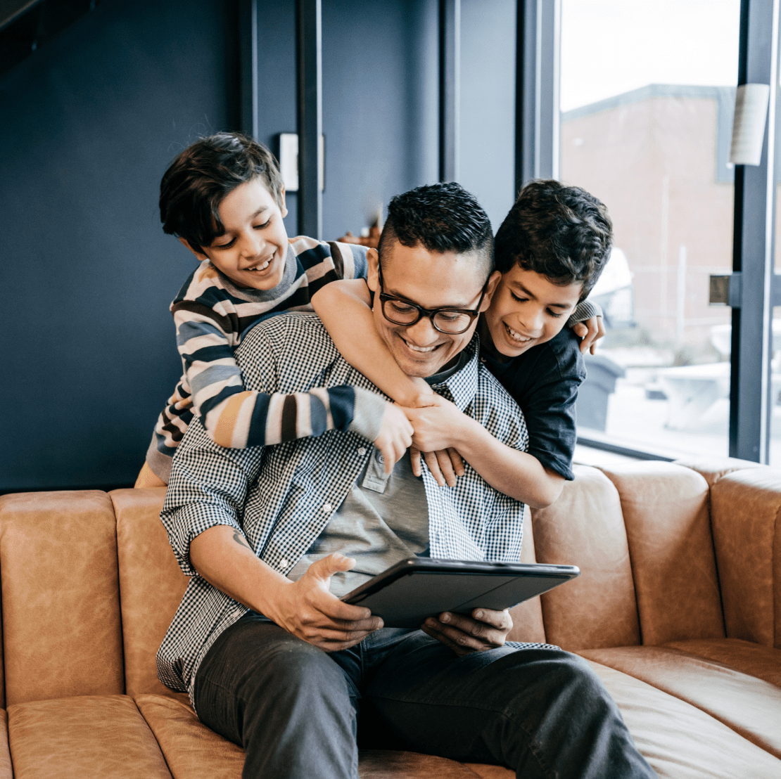 A man and two boys sitting on a couch, looking at a tablet together.