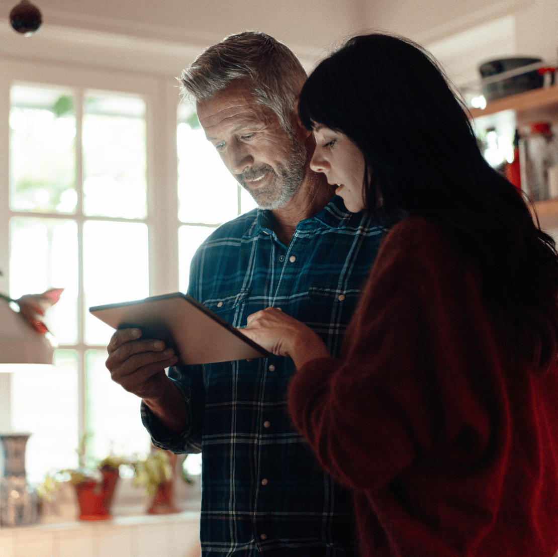 A couple in a kitchen, attentively viewing a tablet together.