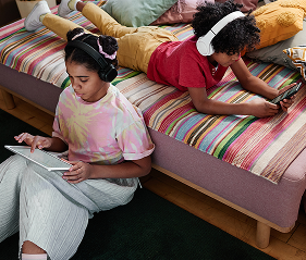 Kids using tablet and phone sitting on couch.