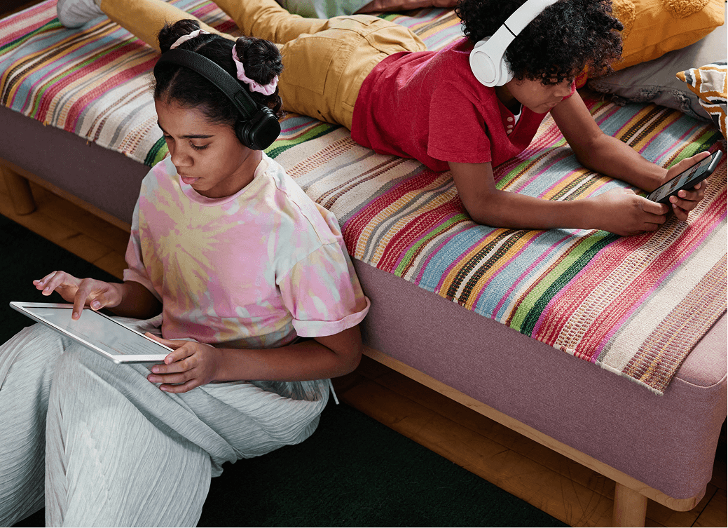 Kids using tablet and phone sitting on couch.